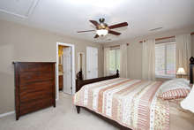 A view of the carpeted master suite, which has a walk-in-closet and ceiling fan. Large windows keep the room bright. 