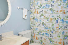 This bathroom offers a tub shower, vinyl flooring, wall lighting and a decorative mirror over the sink vanity. 